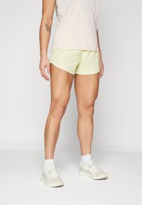 Pantalones cortos deportivos de color amarillo claro con un patrón texturizado, combinados con una parte superior de color claro y zapatillas blancas con acentos en menta.