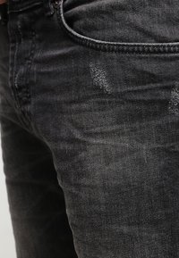 Primer plano de unos vaqueros de mezclilla negros con textura desgastada y ligeras zonas desgastadas cerca del bolsillo frontal y la parte del muslo.