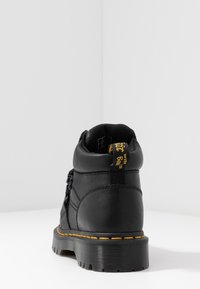 Černé kožené kotníkové boty s texturovaným povrchem, žlutým prošíváním a poutkem s nápisem "s Bouns". Tlustá černá podrážka s drážkami.