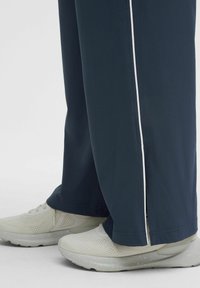 Tamno plave atletske hlače s bijelim bočnim trakama, od lagane tkanine, ravnog kroja, u kombinaciji s svijetlim, teksturiranim atletski cipelama.