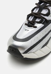 Sølv- og svart joggesko med teksturert overdel, nettseksjoner, svarte snøringer og polstret såle for demping og støtte.
