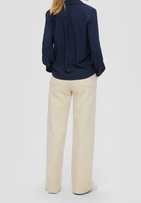 Marineblaues Langarmshirt mit einem Rückenfalte, kombiniert mit cremefarbenen Weitbein-Hosen und weißen Sneakern, die flache Taschen und ein schlichtes Design zeigen.