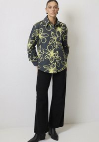 Hallituselised shirt halli värviga, millel on kollased lilled, nööpidega sulgumisvariant, pika varruka disain. Koos mustade laia säärega pükste ja kontsakingadega.