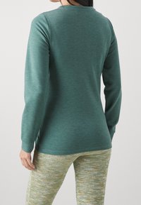 Långärmad grönblå topp i mjukt tyg, med rundad halsringning och slät yta, i kombination med leggings med texturerat mönster i grönt och krämfärgat.