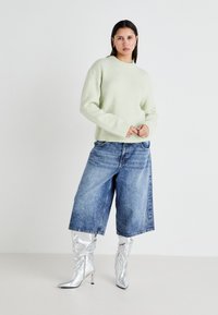 Myntgrønn ullgenser, løstsittende blå denim culotter og metallisk sølvfargede knelengde støvler med spiss tå og glidelåser.
