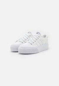 Sneakers bianchi in tela con una robusta suola in gomma bianca, caratterizzati da tre strisce laterali, punta rotonda e chiusura con lacci. Dettaglio di branding sottile.