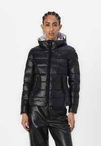 Sort pufferjakke med hætte, lavet af skinnende materiale, med quiltet design, lynlås foran og sidelommer.