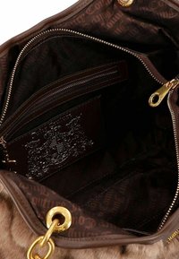 Interior de bolso marrón con bolsillos con cremallera, forro de tela oscura con un patrón de logotipos y tarjetero texturizado con acentos brillantes. Detalles en hardware dorado.