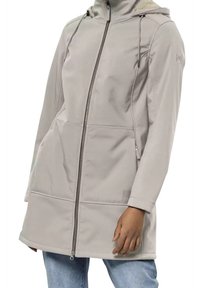 Světle béžový kabát s kapucí, na předním zipu a kapsách, nošený přes modré džíny, odhalující torzo a část paží.