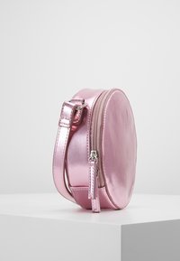 Bolso redondo metálico de color rosa con cierre de cremallera, base plana y correa ajustable. Textura suave con un acabado brillante.