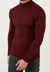 Burgunderfarbener Rippstrick-Pullover mit Rollkragen und langen Ärmeln, der eine figurbetonte Passform und ein strukturiertes Muster aufweist. Das Material wirkt weich und dehnbar.
