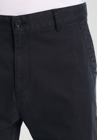 Dark navy pants made of smooth fabric, featuring a button closure, belt loops, and side pockets. Tailored fit with minimal stitching details.