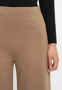 Beige wijde broek gemaakt van soepele stof, met een hoge tailleband met stiksels en een enkele knoopsluiting.