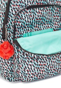 Backpack featuring a colorful pattern of black and red shapes on a light blue background, with a turquoise lining and a red fluffy pom pom keychain.
