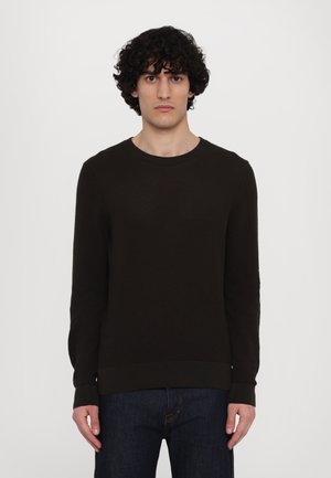 Pull en maille texturé marron foncé avec un col rond et des manches longues, doté d'un ourlet et de poignets côtelés, associé à un jean noir.