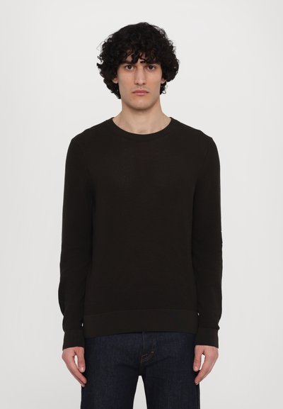 Pull en maille texturé marron foncé avec un col rond et des manches longues, doté d'un ourlet et de poignets côtelés, associé à un jean noir.