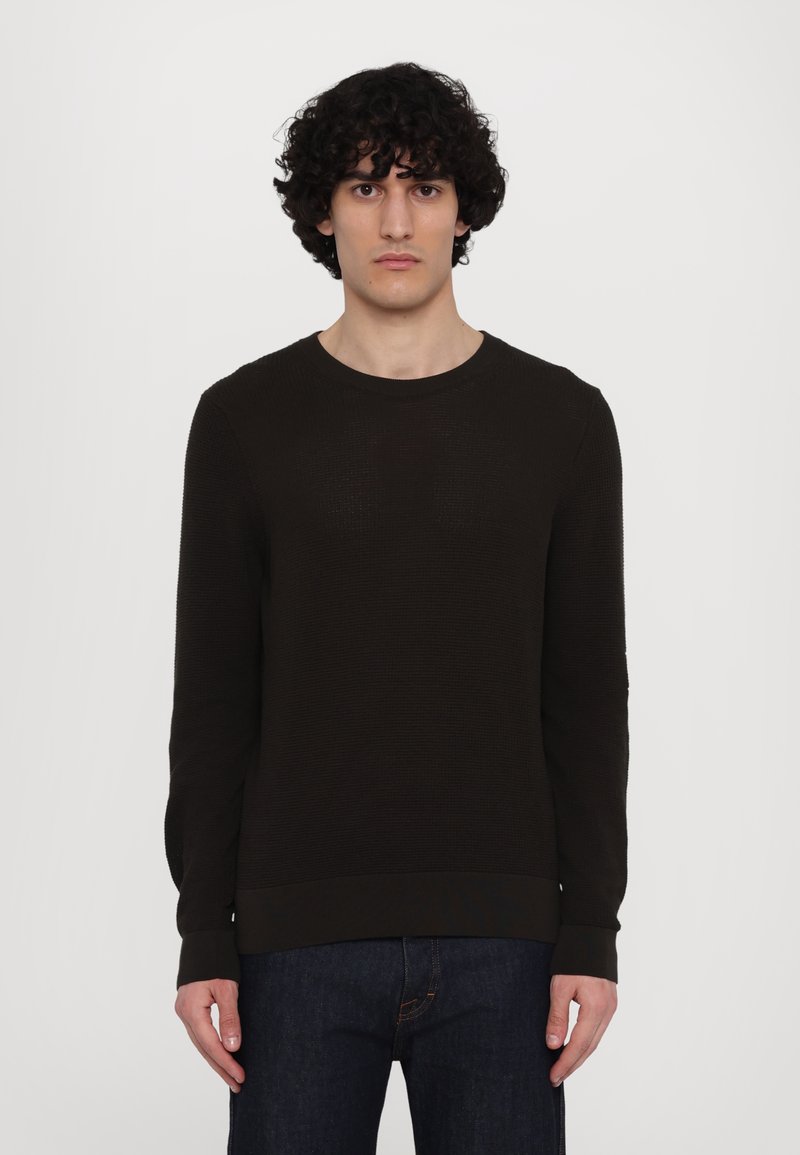Dunkelbrauner strukturierter Pullover mit Rundhalsausschnitt und langen Ärmeln, mit geripptem Saum und Bündchen, kombiniert mit dunkler Jeans.