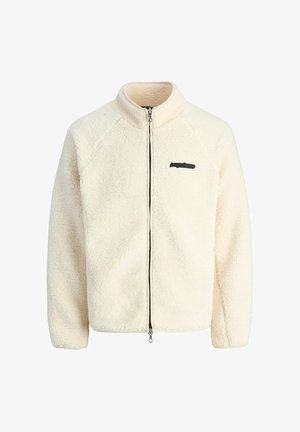 Cremefarbener Fleece-Jacke mit hohem Kragen, Reißverschluss vorne und schwarzem Logoakzent auf der Brust. Sie hat eine weiche, strukturierte Oberfläche.