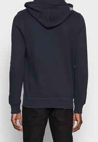 Granatowy hoodie z przednią kieszenią kangurką, z prążkowanymi mankietami i dołem. Posiada okrągły kaptur ze sznurkiem i małe logo z tyłu.