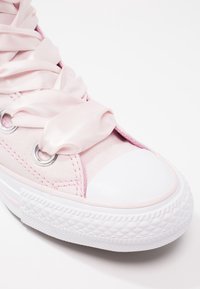 Ljusrosa canvas sneakers med satinband som snörning, silverfärgade öglor och vitgummikork och sula. Ytan är slät med synliga sömmar.