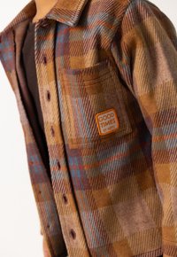 Bruine en oranje geruite flanellen overhemd met een voorzak en een "GOOD TIMES" label, featuring een gestructureerde stof die lijkt op wol en knoopsluiting.