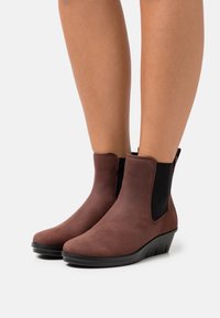 Bottes de cheville en cuir marron avec des panneaux latéraux élastiques et un talon compensé, présentant une texture lisse et un design à bout arrondi.