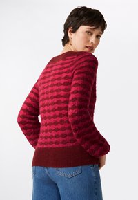 Strickpullover in Pink mit einem strukturierten Rautenmuster, ausgestattet mit einem bordeauxfarbenen Saum und Bündchen. Lange Ärmel und ein abgerundeter Ausschnitt.