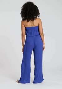 Mono azul sin tirantes con un cuerpo suelto y fruncido, y diseño de pierna ancha. Fabricado en una tela texturizada, que presenta una cinturilla elástica.