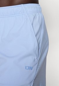 Lysblå atletiske shorts med elastisk talje, der har perforeret tekstur og "ICIW" logo i en mørkere nuance på siden.