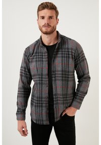 Pilkas ir juodas plaid marškiniai su raudonais akcentais, pagaminti iš minkštos medžiagos. Ilgos rankovės ir smailus apykaklė, dėvimi ant juodos marškinėlių.