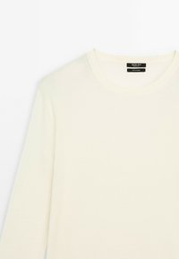 Crème-kleurige, lange mouwen gebreide trui met een ronde hals. Heeft een gladde textuur en een label aan de binnenkant van de hals.