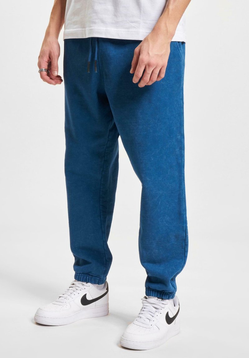 Blue sweatpants with a soft texture, elastic cuffs, and a drawstring waist, paired with white sneakers featuring a black logo.