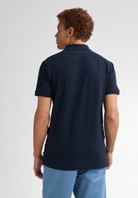 Mjölkblå polo t-shirt med klassisk krage och korta ärmar, med en slät textur och rak fåll, i kombination med ljusblå byxor.