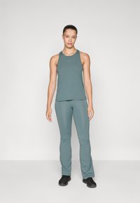 Lichtgroene atletische tanktop en strakke broek, gemaakt van zachte stof met minimale naden. Met een logo op de top. Zwarte schoeisel.