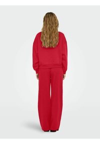 Κόκκινη μπλούζα με στρογγυλή λαιμόκοψη και παντελόνι σε φαρδύ κόψιμο, φτιαγμένα από μαλακό ύφασμα. Η μπλούζα έχει ριχτούς ώμους, ενώ το παντελόνι διαθέτει ελαστική μέση.