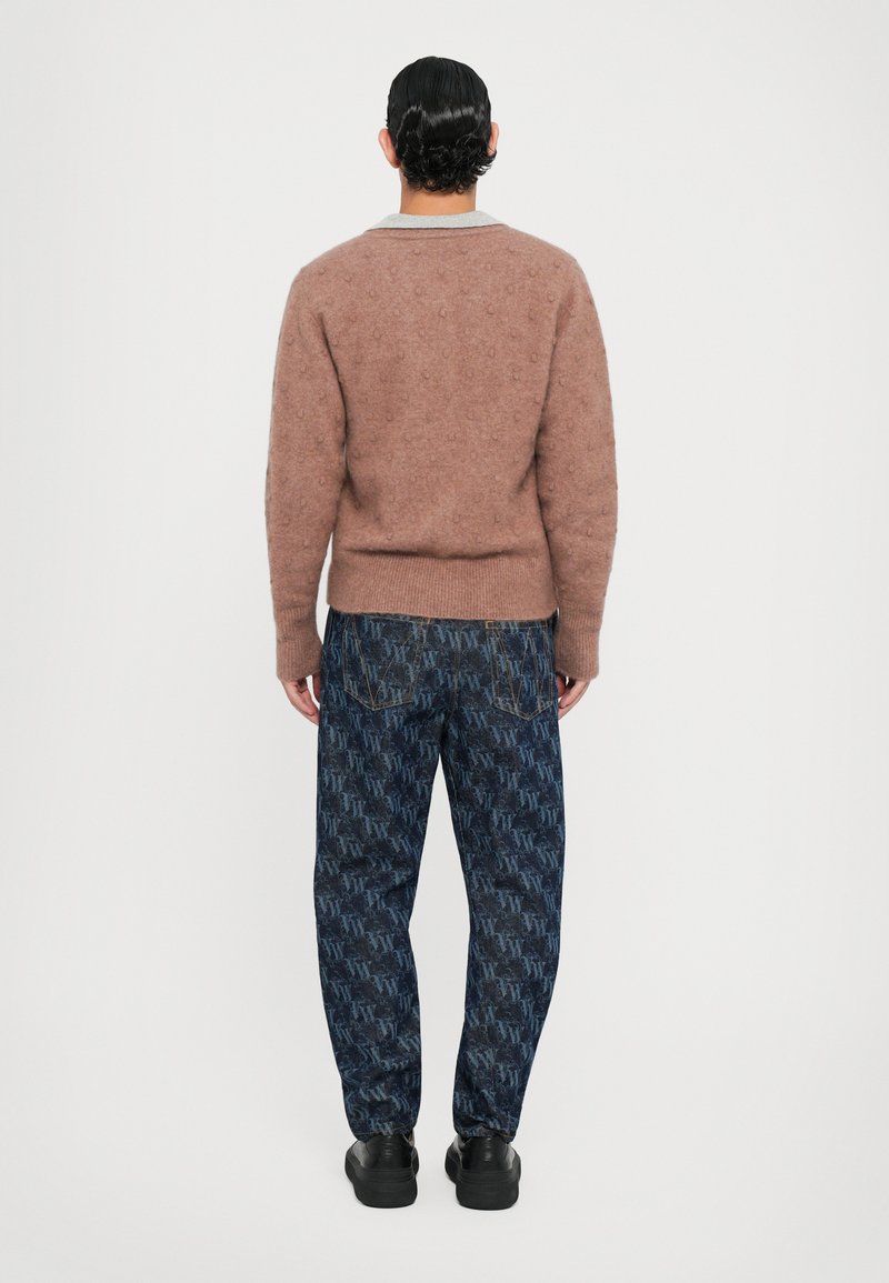 Bruine gebreide trui met textuurstippen en een grijze kraag, gecombineerd met donkerblauwe gebloemde jeans en zwarte sneakers. Van achter bekeken.