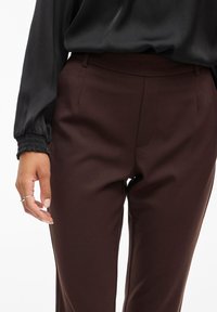 Burgundijas krāsas pielāgotas bikses ar gludu faktūru, ar vidēja pacēluma jostu, sānu kabatām un šauru piegriezumu.