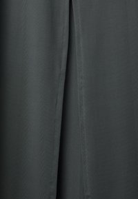 Donkergroene stof met een gladde textuur, met een verticale splitdetail langs het midden. Het ontwerp is minimalistisch met strakke lijnen.