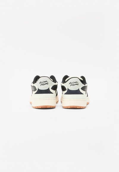 Zapatillas con un upper suave en negro y crema, con un diseño de cuero y textil, cuello acolchado y suela de goma con un acento naranja.