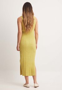 Robe débardeur jaune côtelée de longueur midi, avec des fentes latérales et une coupe ajustée, confectionnée dans un tissu en maille doux et texturé.