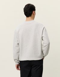 Pilkos spalvos medvilninė megzta palaidinė su ilgomis rankovėmis, išsipūtusiais rankogaliais ir apačia, bei apvalia kaklo iškirpte. Atgalinis vaizdas rodo lygią tekstūrą ir laisvą, patogią formą.