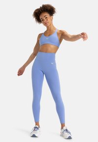 Lichtblauwe sportbeha en high-waisted leggins, met een gladde textuur en subtiele logo, gecombineerd met witblauwe sportschoenen.
