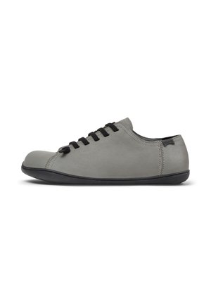 Zapatilla gris con punta redonda, cordones negros y suela negra, ubicada sobre un fondo blanco. Textura de cuero suave visible.