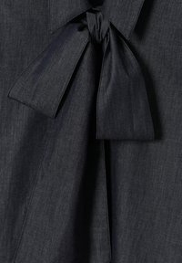 Tmavomodrý rifľový top s detailom v podobe mašle. Hladká textúra, štruktúrovaný golier a široké stuhy vytvárajú upravený vzhľad.