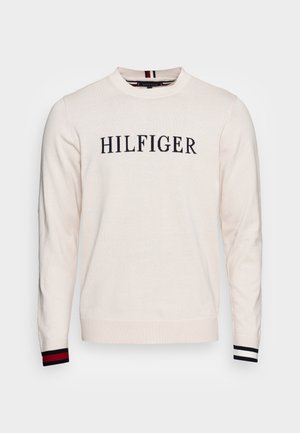 Kremowy sweter z okrągłym dekoltem z napisem "HILFIGER" na przodzie, ściągacze z prążkami w czerwono-biało-czarne paski na rękawach.