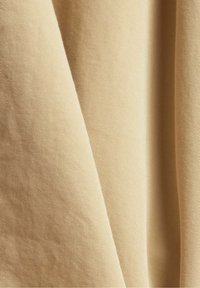 Tissu beige avec une surface texturée et côtelée, présentant une chute douce et un léger éclat, plié pour mettre en valeur la dimensionnalité et le motif.