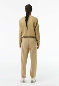 Beige kort sweatshirt och matchande joggers, med en bakficka, mudd nederkant och textilstruktur. Sneakers med grå och gula accenter.