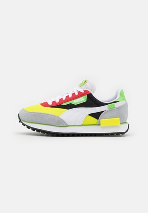 Niskie buty sportowe Puma w kolorach żółtym, czerwonym, czarnym, białym, szarym i zielonym z białymi sznurowadłami i gumową podeszwą na białym tle.