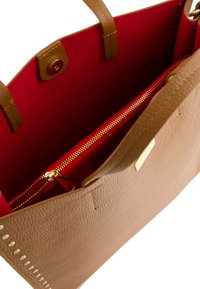Sac fourre-tout en cuir texturé tan avec intérieur rouge, doté de fermetures éclair et de détails en matériel doré, et de poignées plates. Poche zippée à l'intérieur.