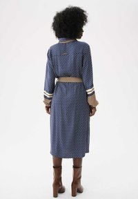 Blaues Polka-Dot-Kleid mit tailliertem Design, langen Ärmeln mit gestreiften Bündchen und einem Kragen. Hergestellt aus leichtem Stoff, mit mittellangem Schnitt.